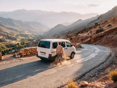 A private driver in Morocco standing beside a clean touring vehicle on a mountain road at golden hour - Morocco driver tours